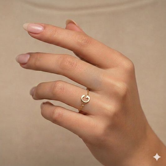 Hand wearing a gold ring with a 'C' on a beige background