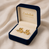 Gold earrings in a 'Embellish' jewelry box on a beige fabric background