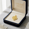 Gold pendant in a 'Embellish Gold Jewelry & Diamond' box on a textured surface