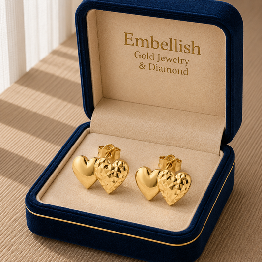 Gold heart-shaped earrings in a 'Embellish' jewelry box on a wooden surface.