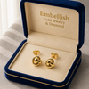 Gold earrings in a 'Embellish Gold Jewelry & Diamond' box on a neutral background
