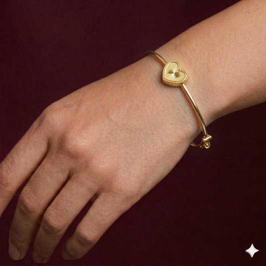 Gold bracelet with a heart-shaped clasp on a wrist against a dark background