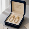 Gold earrings in a 'Embellish Gold Jewelry & Diamond' box on a textured surface.