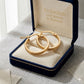 Gold hoop earrings in a 'Embellish Gold Jewelry & Diamond' box on a textured surface.