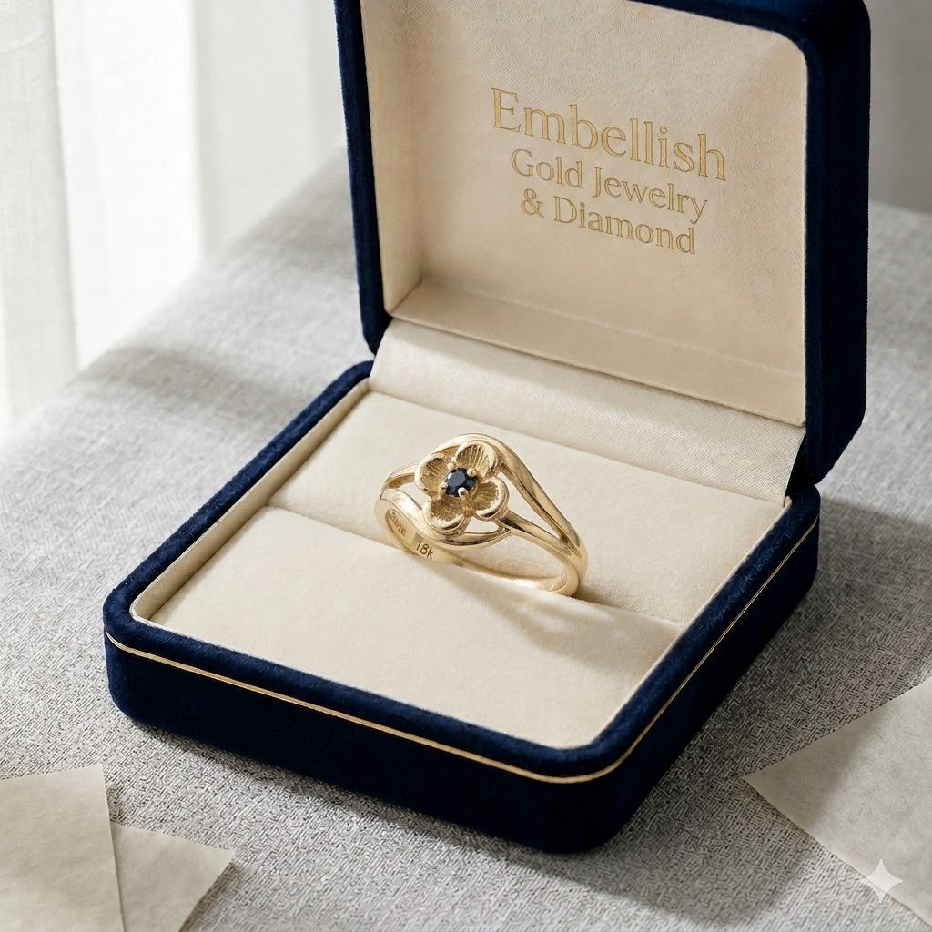Gold ring with a blue gemstone in an open jewelry box labeled 'Embellish Gold Jewelry & Diamond'.