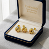 Gold knot earrings in a 'Embellish Gold Jewelry & Diamond' box on a gray surface.