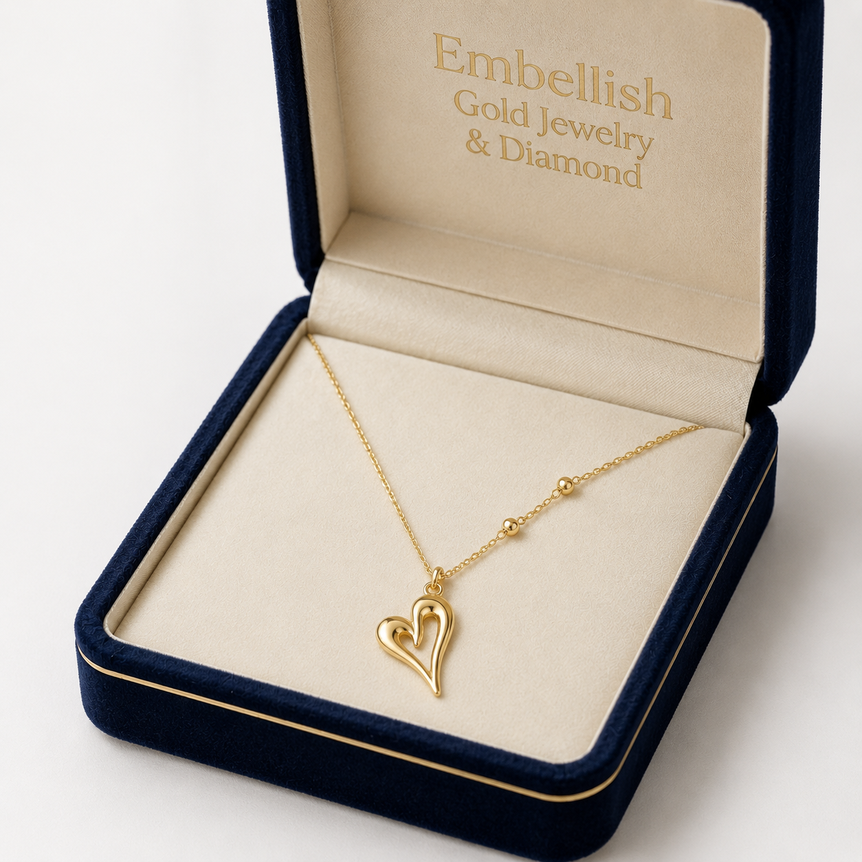 Gold heart necklace in an open jewelry box with 'Embellish Gold Jewelry & Diamond' branding.