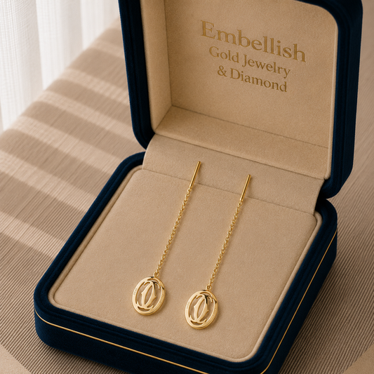 Gold earrings in a 'Embellish Gold Jewelry & Diamond' box on a textured surface.