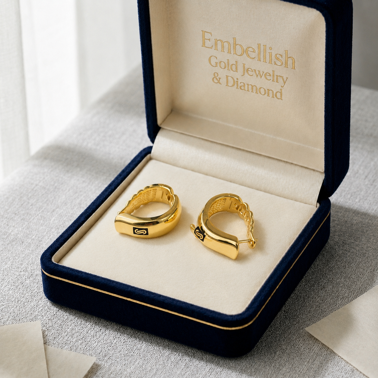 Gold hoop earrings in a 'Embellish Gold Jewelry & Diamond' box on a light surface.