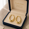Gold hoop earrings in a 'Embellish Gold Jewelry & Diamond' box on a beige surface.