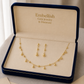 Gold jewelry set including necklace and earrings in an 'Embellish' box.