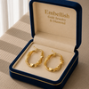 Gold hoop earrings in a 'Embellish Gold Jewelry & Diamond' box on a textured surface.