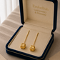 Gold earrings in a 'Embellish Gold Jewelry & Diamond' box on a textured surface.