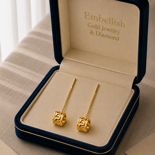 Gold earrings in a 'Embellish Gold Jewelry & Diamond' box on a textured surface.