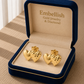 Gold heart-shaped earrings in a 'Embellish' jewelry box on a wooden surface.