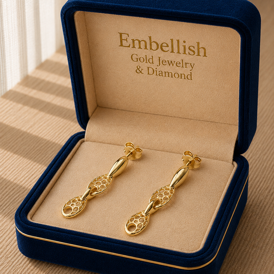 Gold earrings in a 'Embellish Gold Jewelry & Diamond' box on a wooden surface.