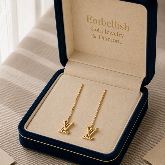 Gold earrings in a 'Embellish Gold Jewelry & Diamond' box on a neutral background