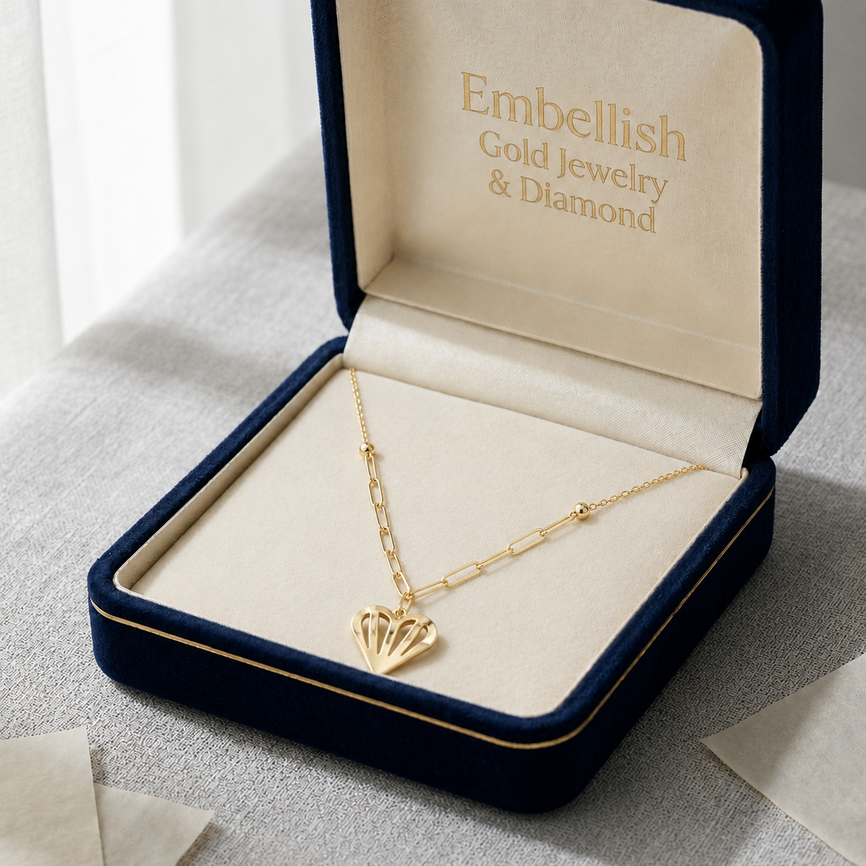 Gold necklace with a heart pendant in an open jewelry box labeled 'Embellish Gold Jewelry & Diamond'.