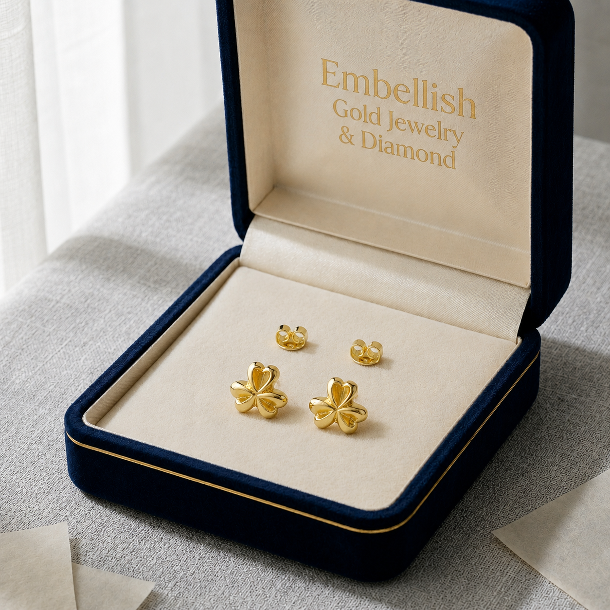 Gold earrings in a 'Embellish Gold Jewelry & Diamond' box on a light background