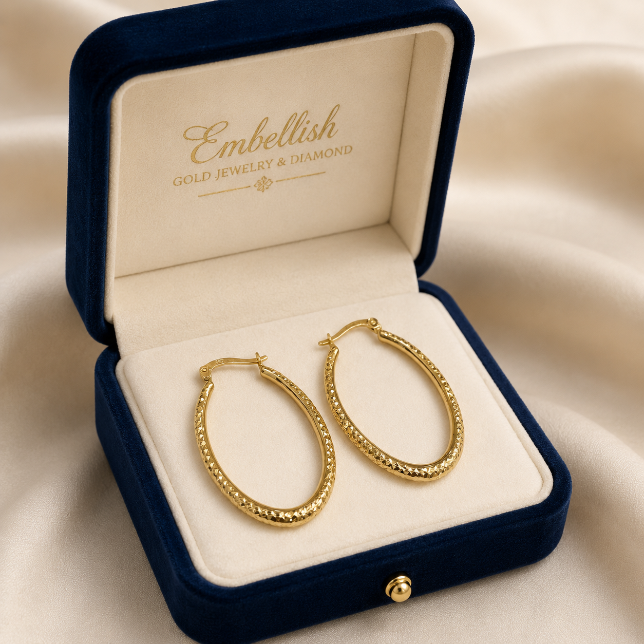 Gold hoop earrings in a 'Embellish' jewelry box on a beige fabric background
