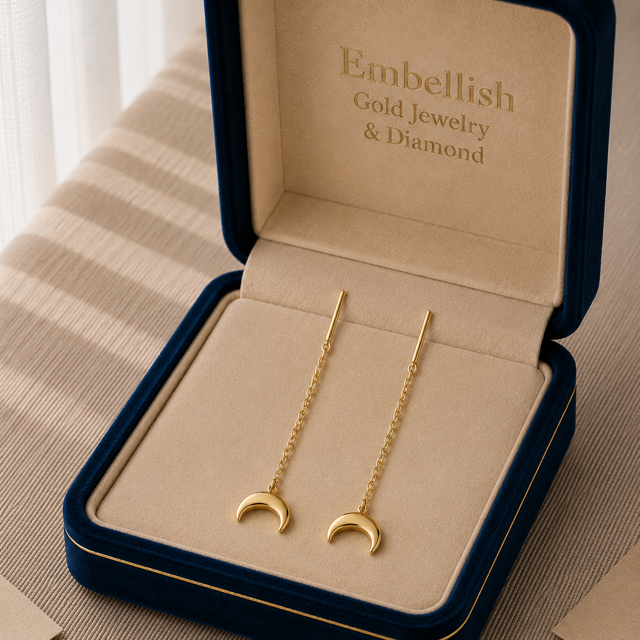 Gold moon-shaped earrings in a 'Embellish' jewelry box.