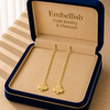 Gold earrings with clover charms in an 'Embellish' jewelry box.
