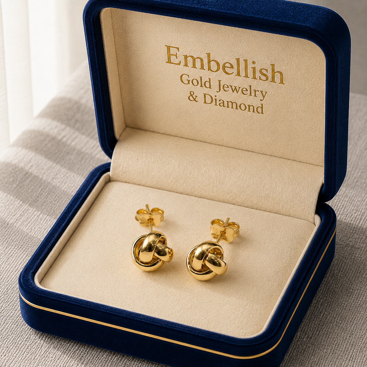 Gold earrings in a 'Embellish Gold Jewelry & Diamond' box on a neutral background