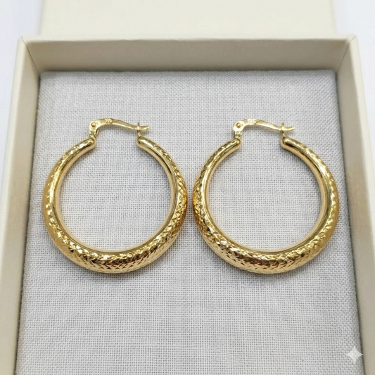 Gold hoop earrings on a gray fabric surface