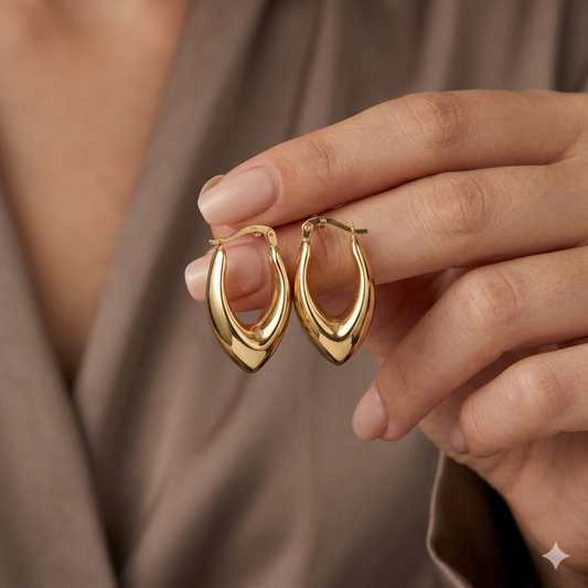 Gold hoop earrings held by a hand against a neutral background