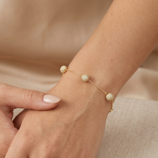 Gold bracelet with pearl-like beads on a wrist against a neutral background