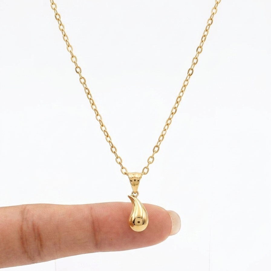 Gold necklace with a small pendant held by a finger on a white background