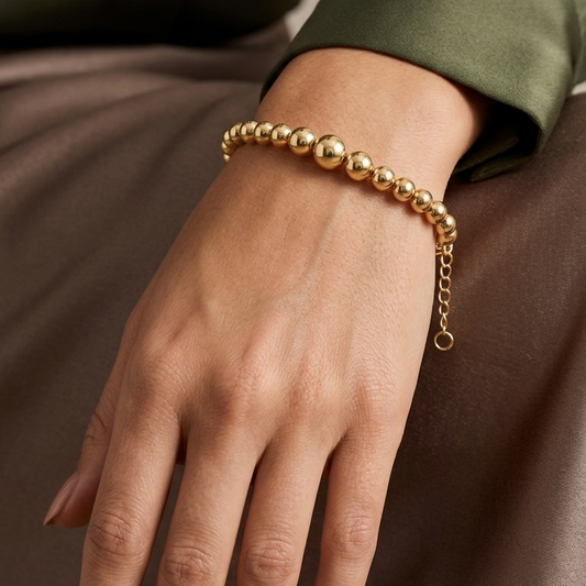 Gold beaded bracelet on a wrist with a neutral background