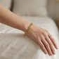 Gold bracelet and ring on a hand against a neutral background