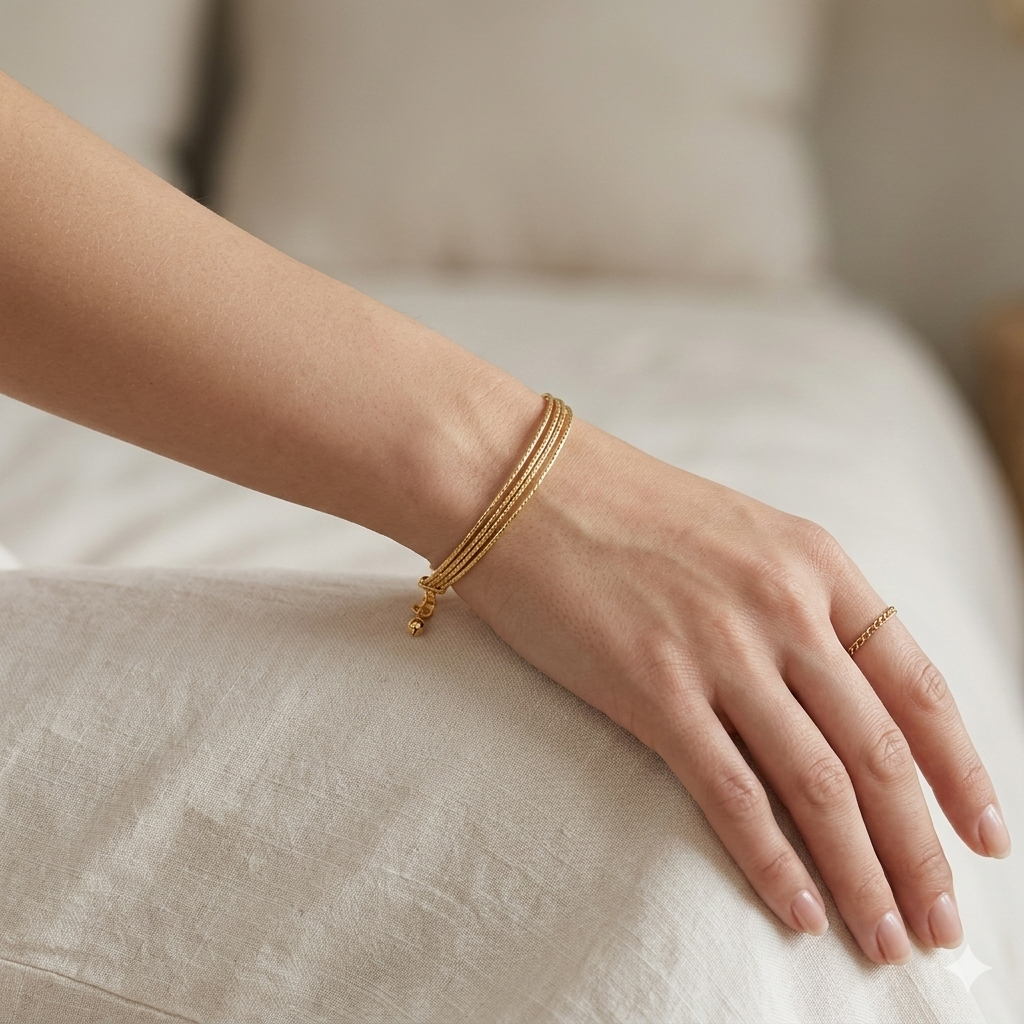 Gold bracelet and ring on a hand against a neutral background