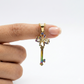 Gold key-shaped pendant with colorful accents held between fingers against a white background