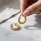 Gold hoop earrings held by a hand on a light background