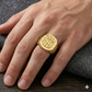 Gold ring with a logo on a person's hand against a dark background