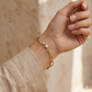 Gold chain bracelet on a wrist with a neutral background