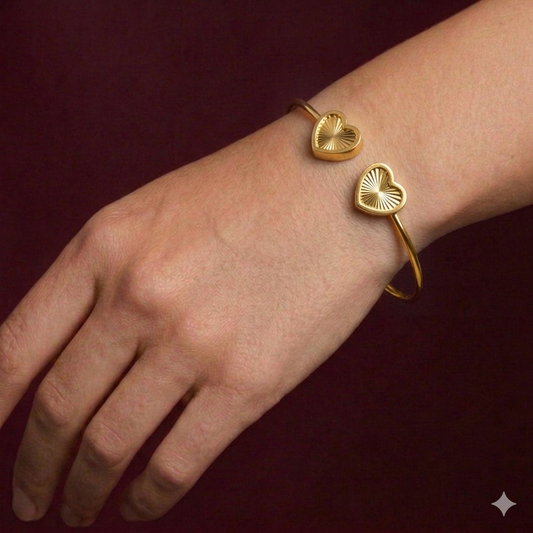 Gold bracelet with heart-shaped ends on a wrist against a dark red background