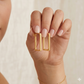 Gold hoop earrings being worn on a hand with a neutral background