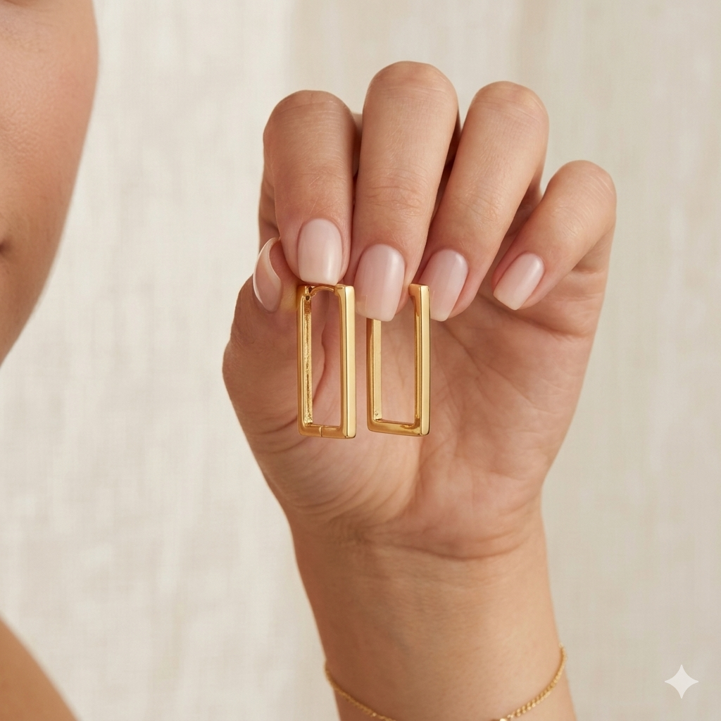 Gold hoop earrings being worn on a hand with a neutral background