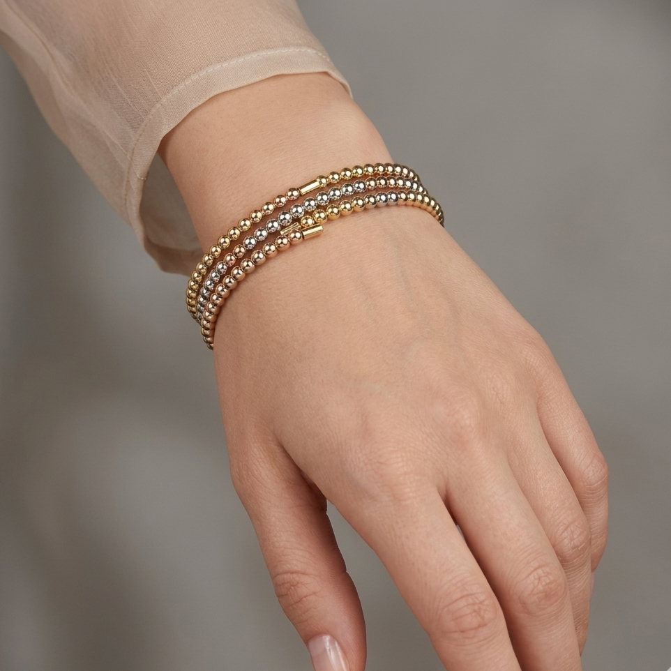 Hand wearing three gold bracelets on a neutral background