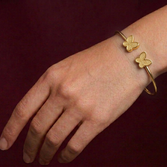 Gold butterfly bracelet on a wrist against a dark background