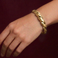 Gold braided bracelet on a wrist against a dark background