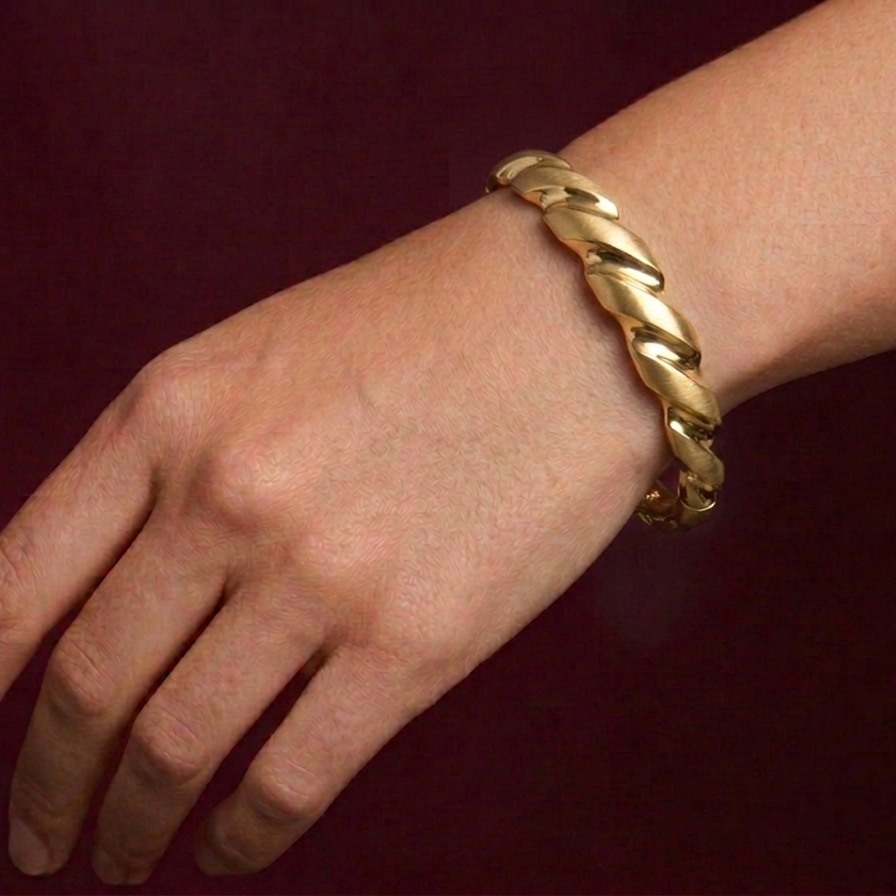Gold braided bracelet on a wrist against a dark background