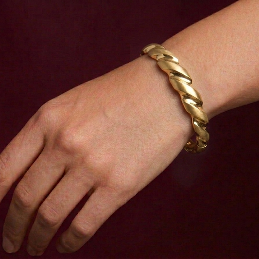 Gold braided bracelet on a wrist against a dark background