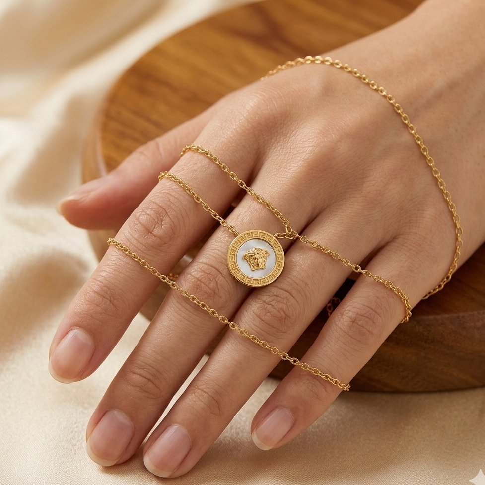 Gold chain bracelet and ring on a hand with a neutral background
