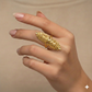 Gold leaf ring on a hand against a beige background