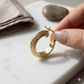 Gold hoop earring held by a hand on a marble surface with a stone in the background