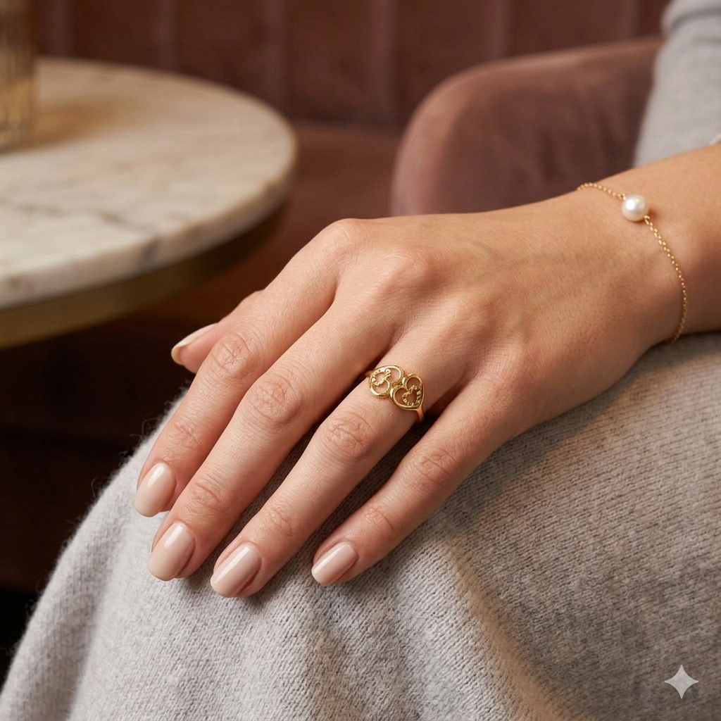 Hand wearing a gold ring with a marble table and brown couch in the background